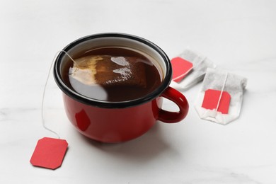 Photo of Tea bags and cup of hot beverage on white table, closeup