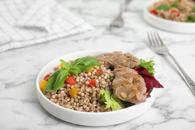 Photo of Tasty buckwheat porridge with meat on white marble table