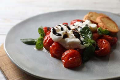 Delicious burrata cheese served with tomatoes, croutons and basil sauce on white wooden table, closeup