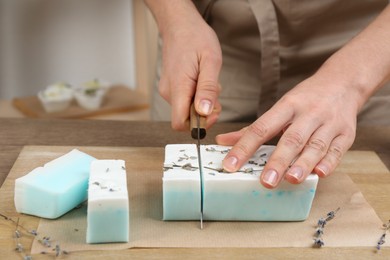Photo of Woman cutting natural handmade soap on wooden table, closeup