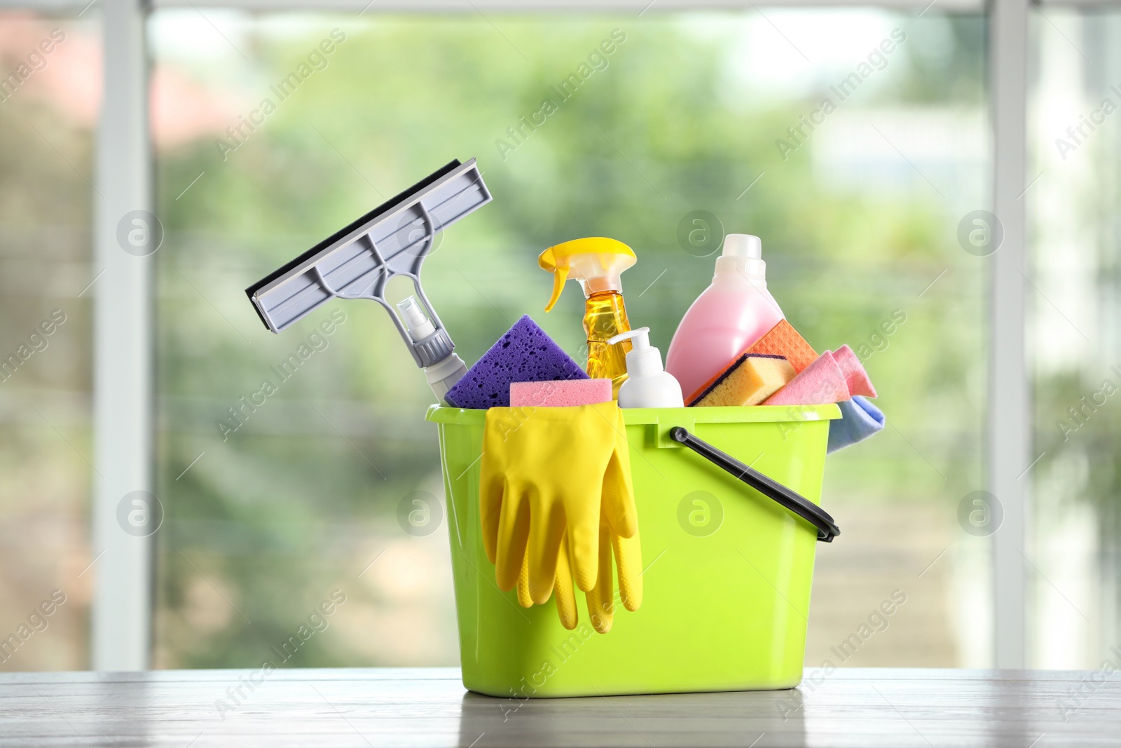 Photo of Light green bucket with cleaning products on wooden table indoors