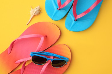 Photo of Flip flops and sunglasses on yellow background, flat lay. Beach accessories
