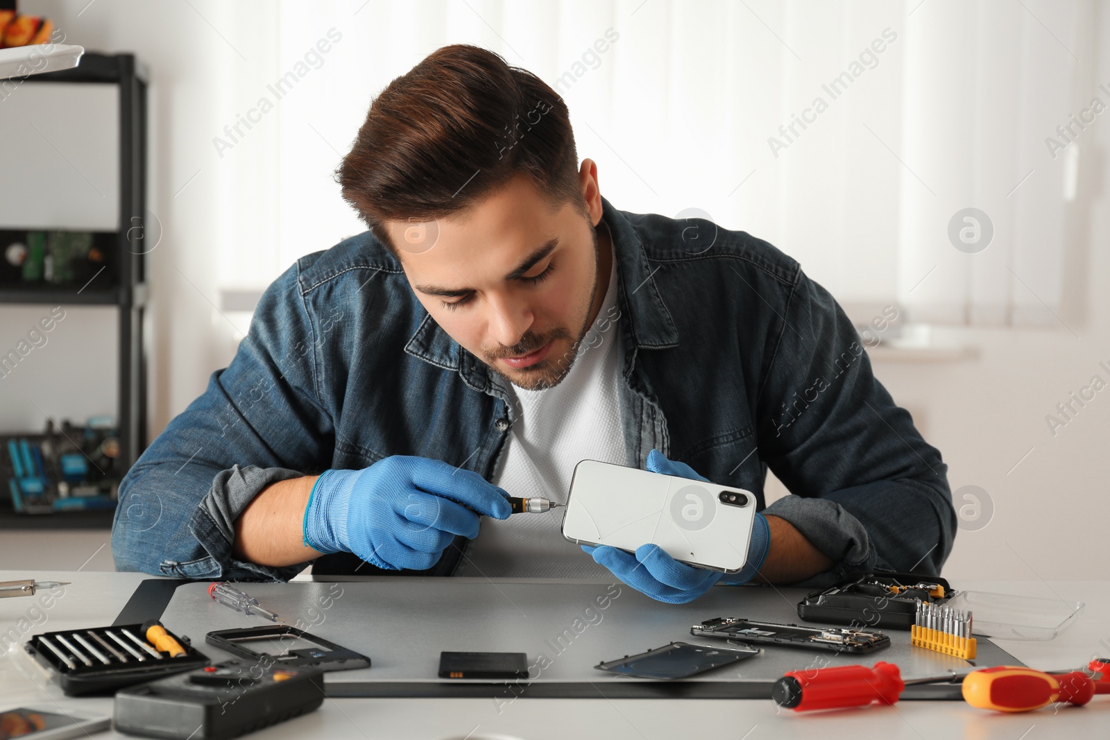 Photo of Technician repairing broken smartphone at table in workshop