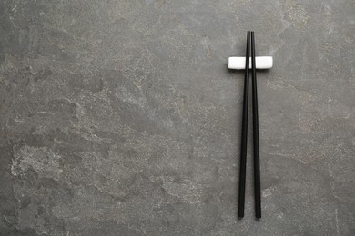 Photo of Pair of black chopsticks with rest on grey table, top view. Space for text