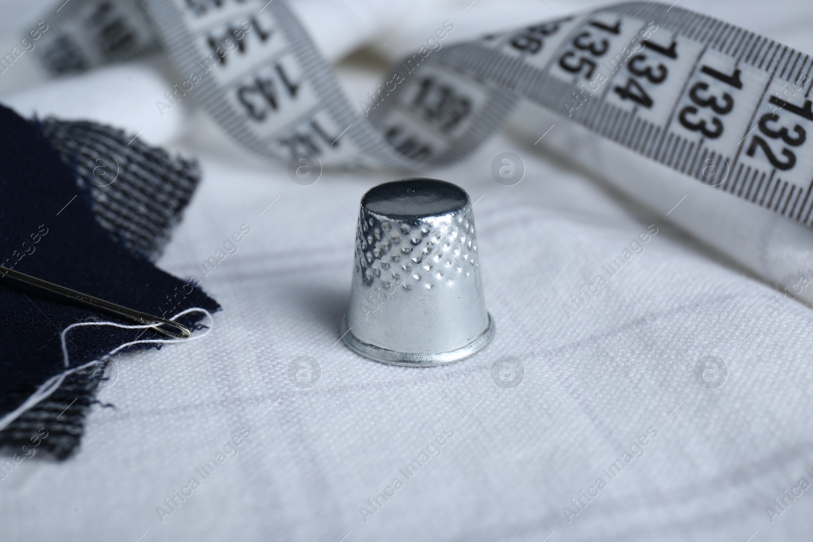 Photo of Silver thimble and other sewing accessories on checkered cloth, closeup