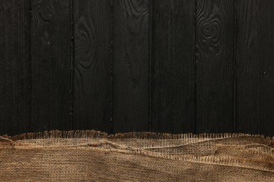 Photo of Burlap fabric on black wooden table, top view. Space for text