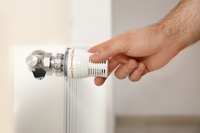 Photo of Man adjusting heating radiator thermostat indoors