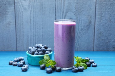 Photo of Glass of blueberry smoothie with mint and fresh berries on blue wooden table