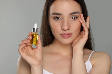 Beautiful young woman with essential oil on light grey background, closeup