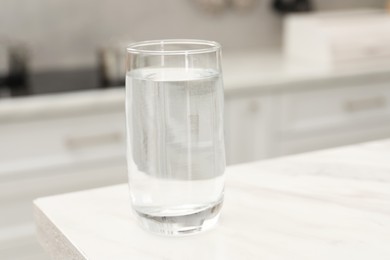 Glass with clear water on white marble table in kitchen