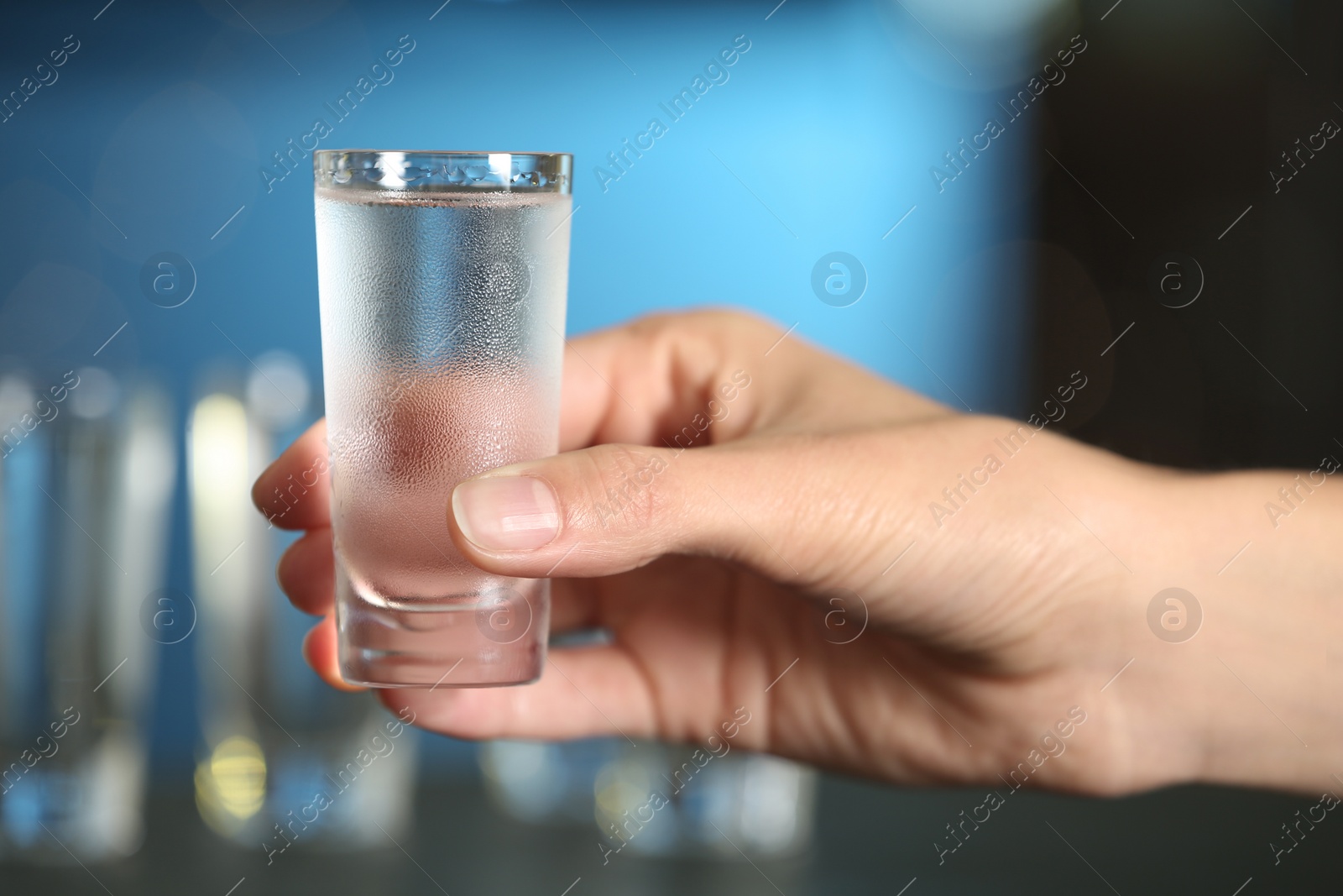 Photo of Woman holding shot of vodka on blurred background, closeup