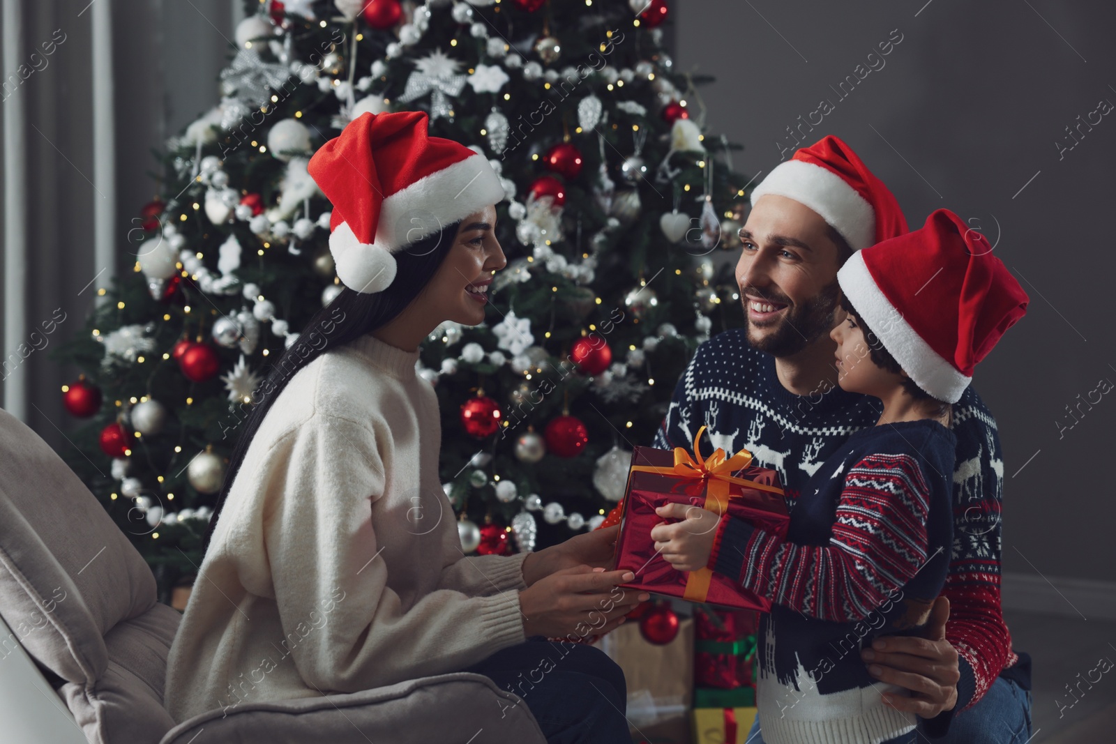 Photo of Father with his cute son presenting gift to mother at home. Christmas celebration