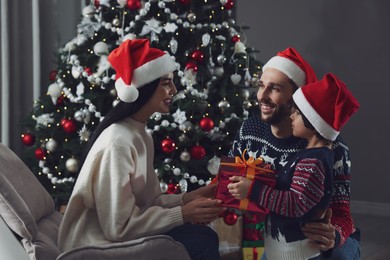 Photo of Father with his cute son presenting gift to mother at home. Christmas celebration