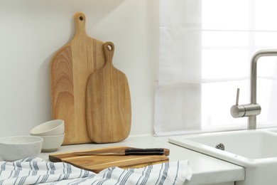 Wooden cutting boards, bowls, knife and towel on white countertop near sink in kitchen