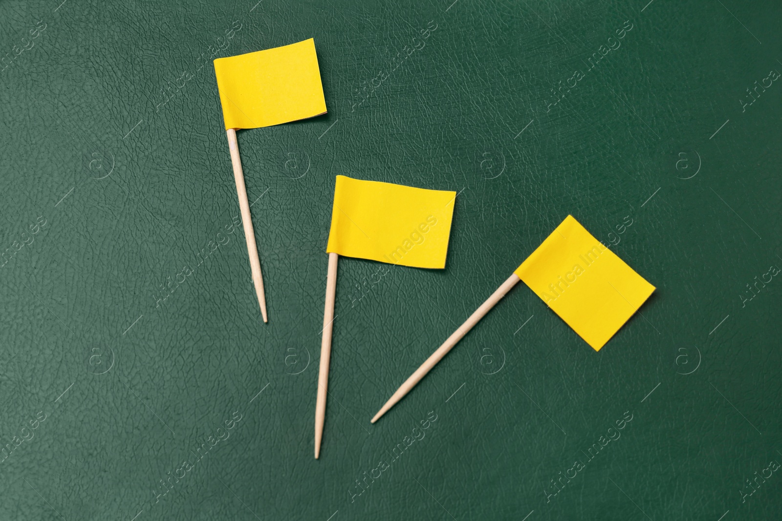 Photo of Small yellow paper flags on green background, flat lay