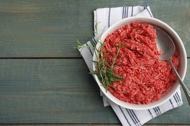 Photo of Fresh minced meat and spoon in bowl on light blue wooden table, top view. Space for text