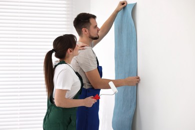 Workers hanging light blue wallpaper in room