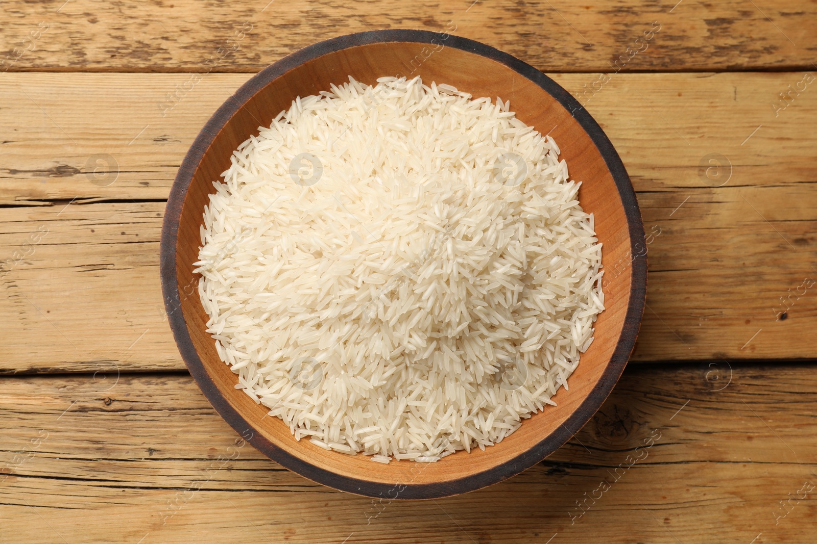 Photo of Raw basmati rice in bowl on wooden table, top view