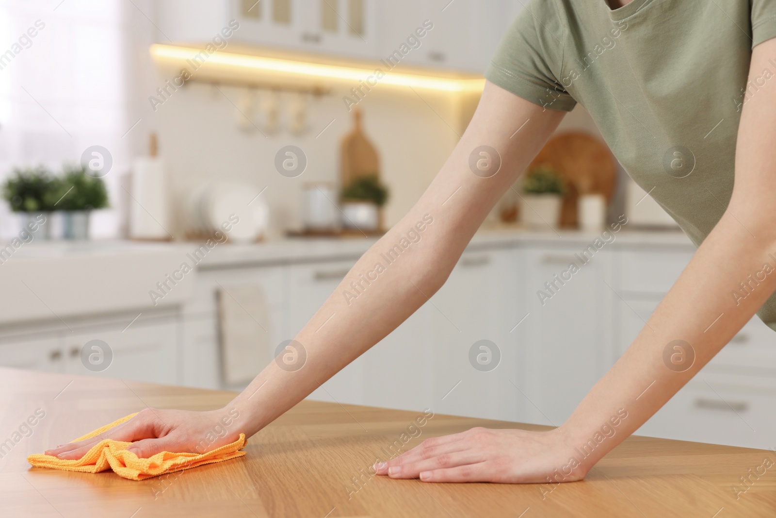 Photo of Woman with microfiber cloth cleaning wooden table in kitchen, closeup