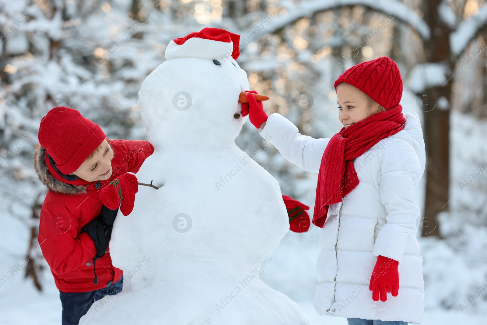 Photo of Cute little girl and boy making snowman in winter park