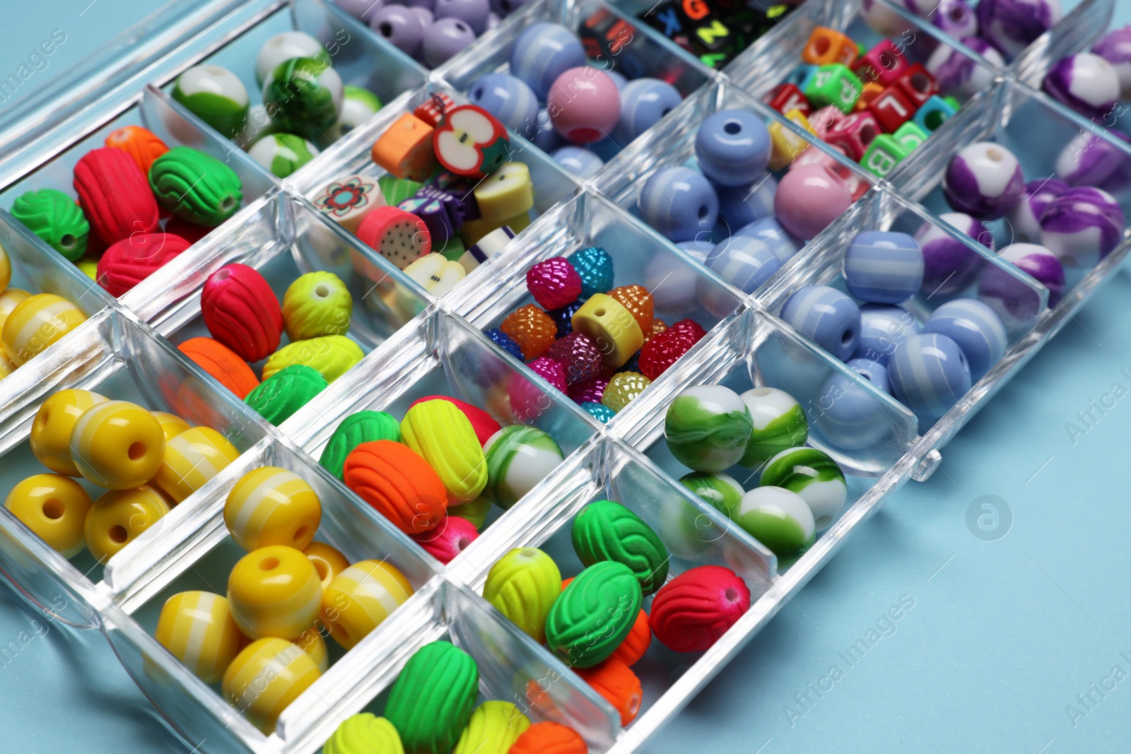 Photo of Box with different colorful beads on light blue background, closeup