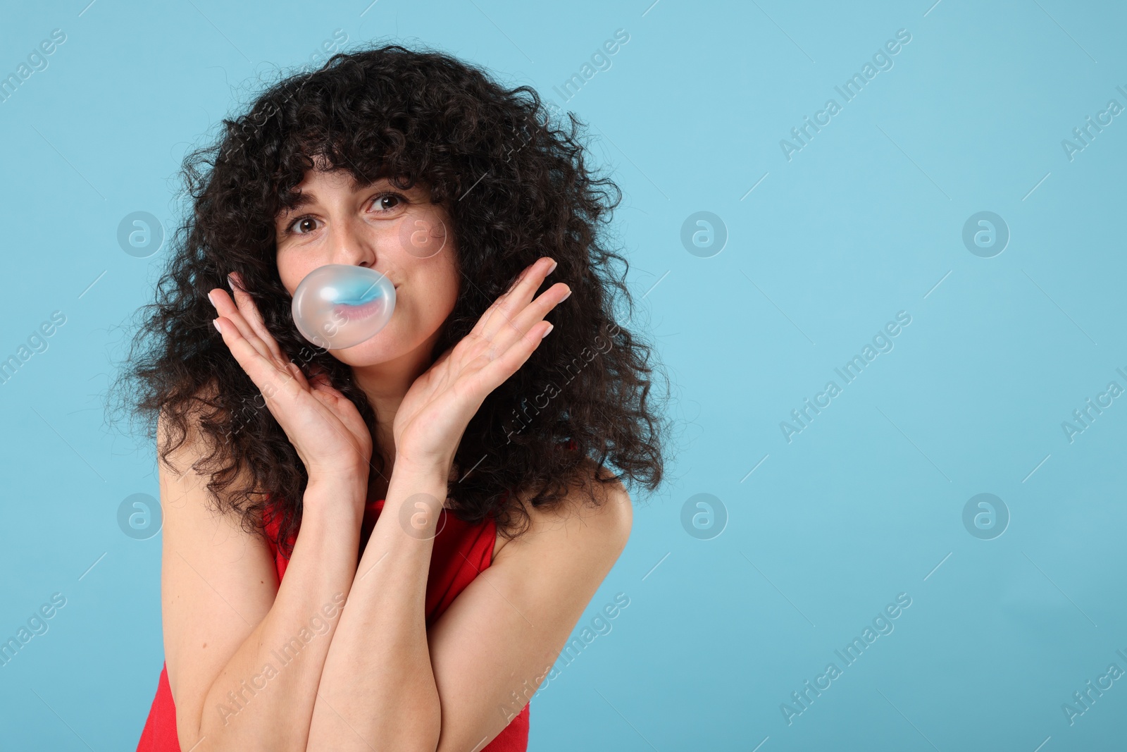 Photo of Beautiful young woman blowing bubble gum on light blue background. Space for text