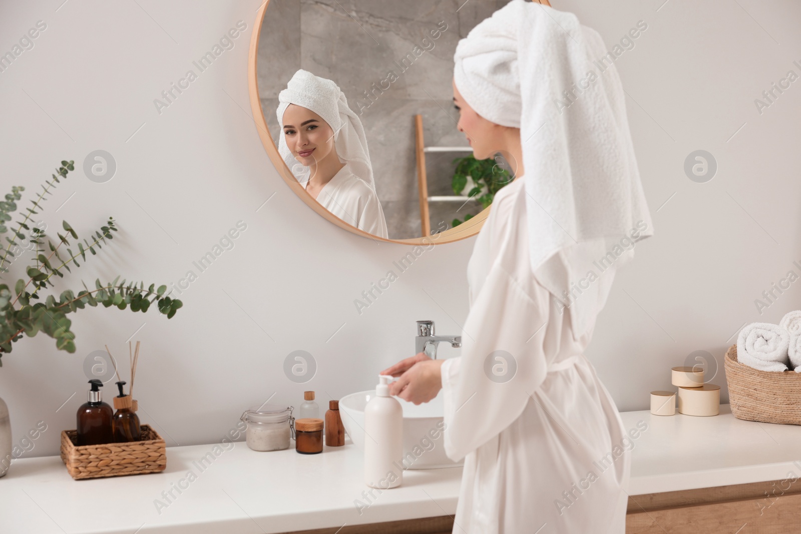 Photo of Beautiful young woman using body cream in bathroom, space for text