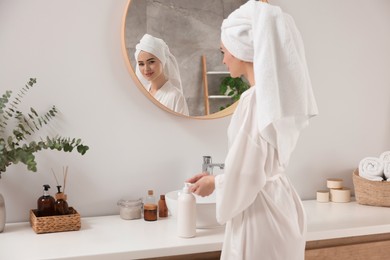 Beautiful young woman using body cream in bathroom, space for text