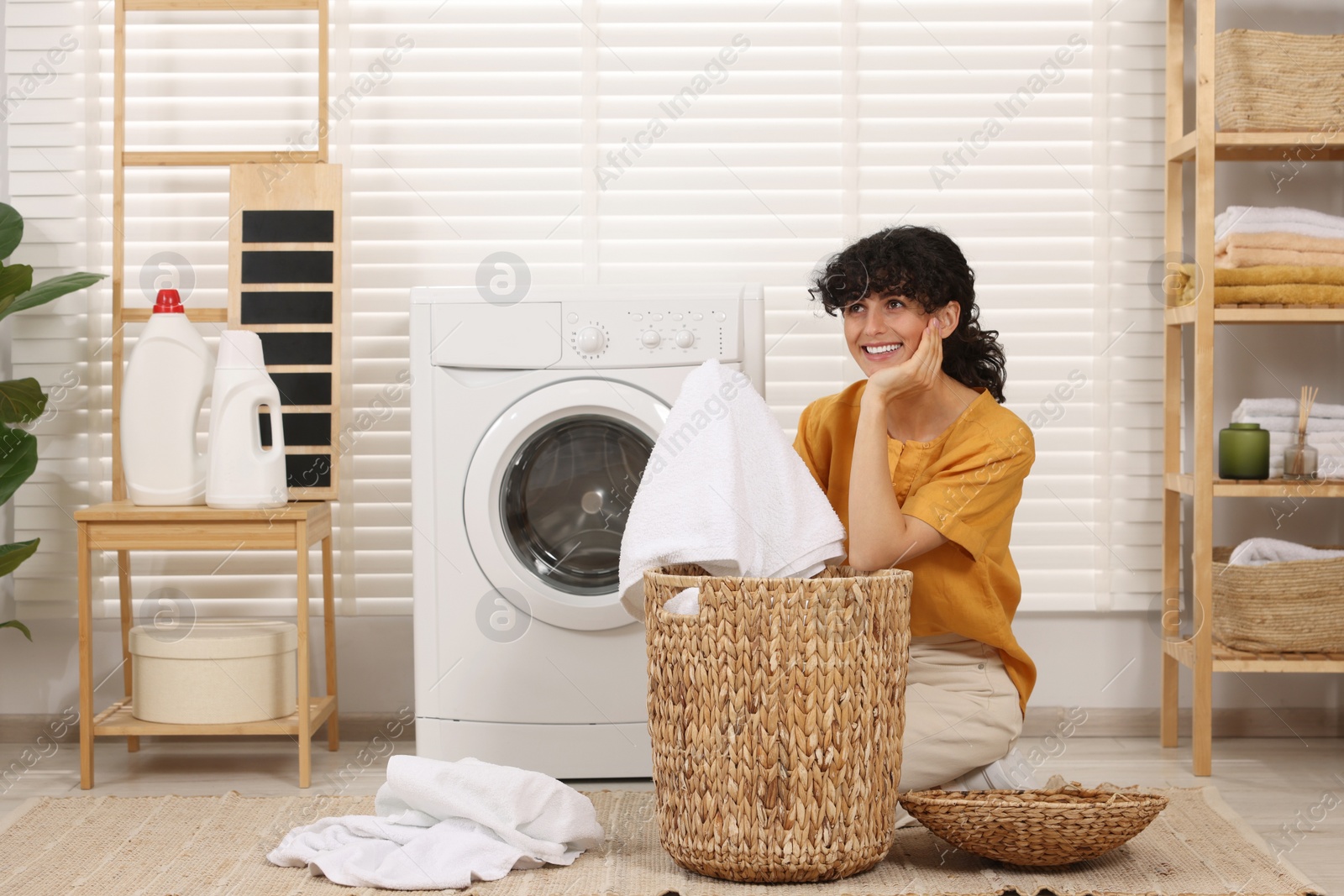 Photo of Happy woman with laundry near washing machine indoors