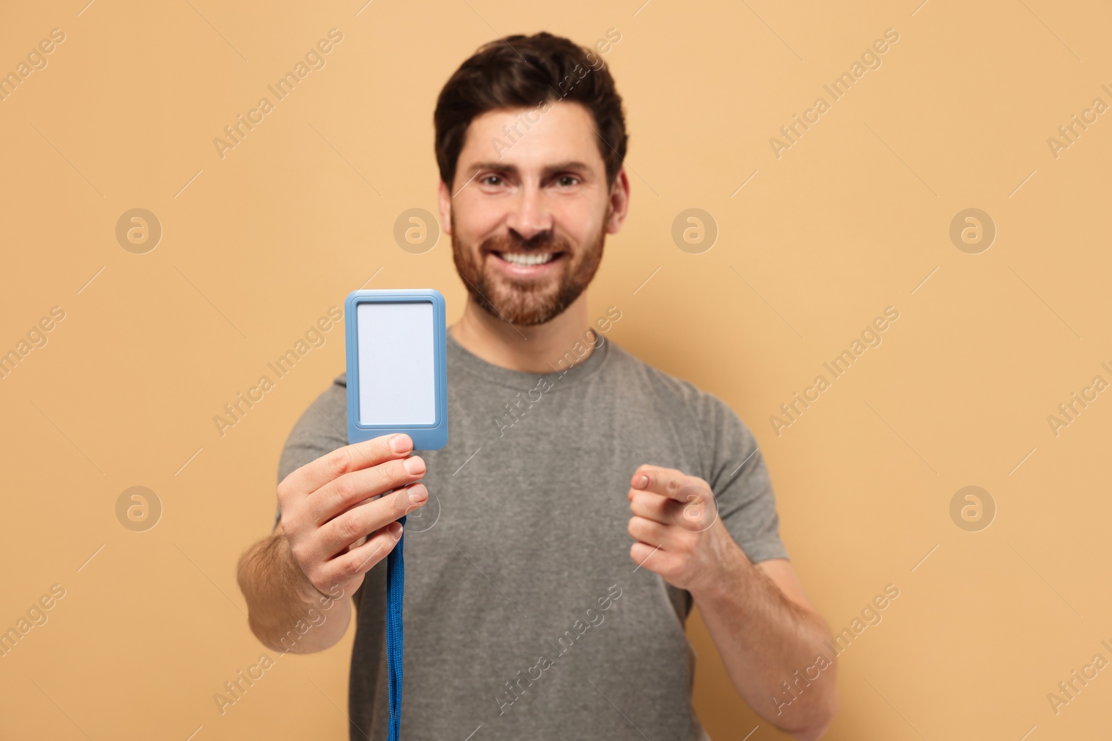 Photo of Happy man showing VIP pass badge against beige background, focus on hand