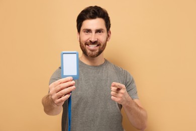Photo of Happy man showing VIP pass badge against beige background, focus on hand