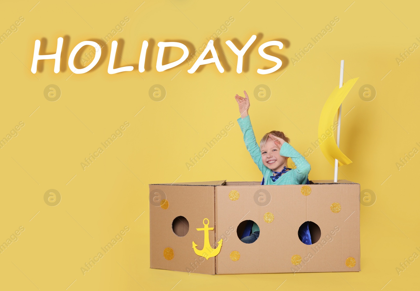 Image of School holidays. Cute little child playing with cardboard ship near yellow wall