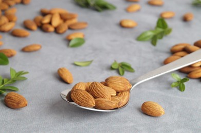 Photo of Spoon with tasty almonds and fresh green leaves on light grey table, closeup