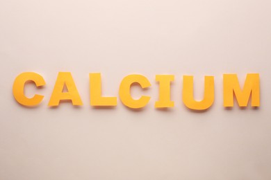 Word Calcium made of orange letters on beige background, flat lay