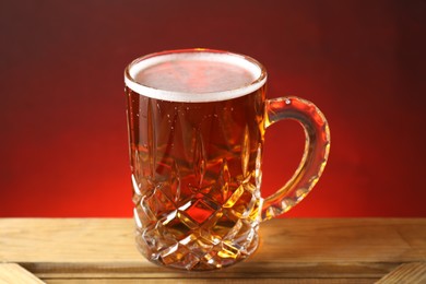 Photo of Mug with fresh beer on wooden crate against color background, closeup