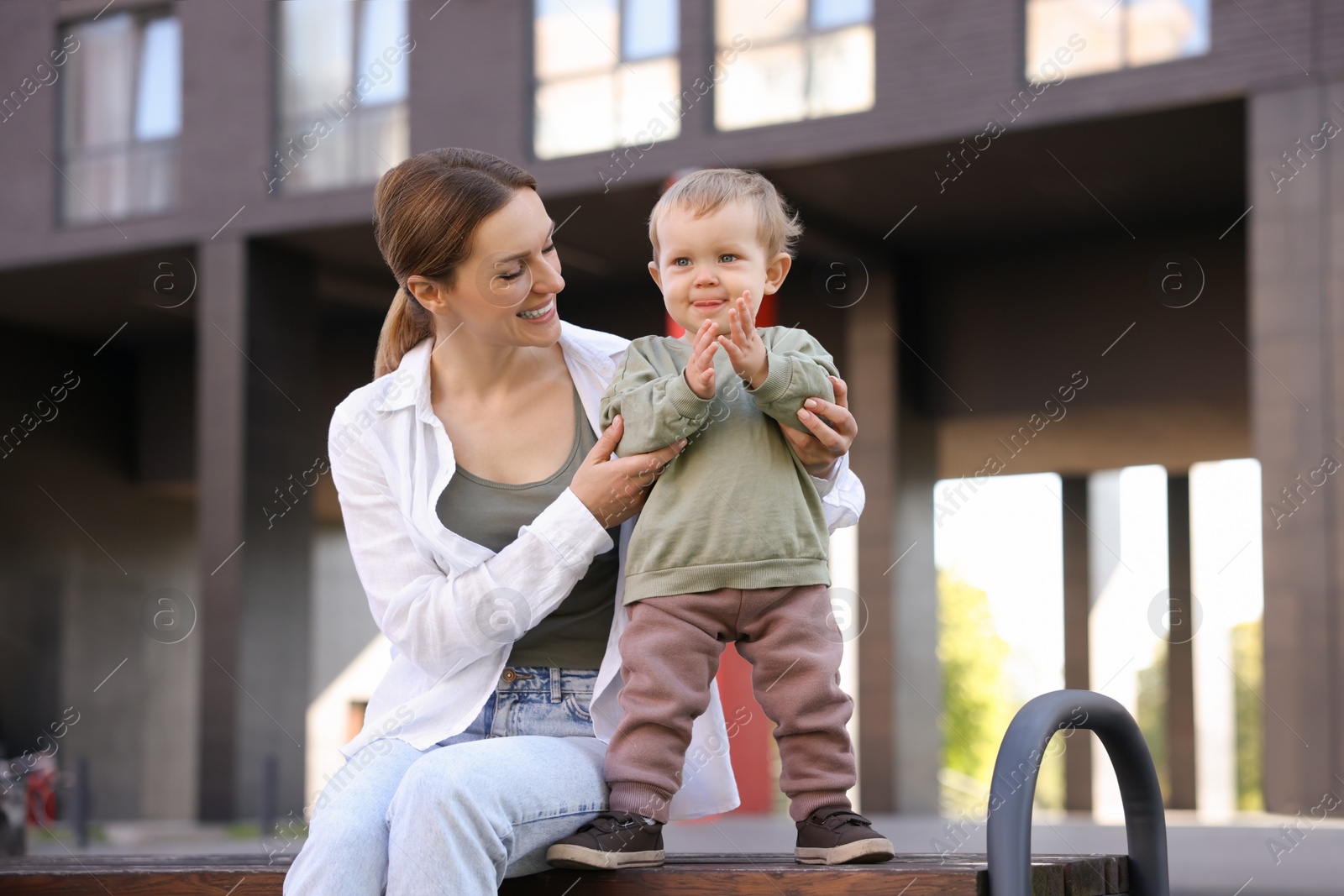 Photo of Happy nanny with cute little boy on bench outdoors