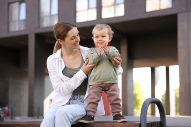 Happy nanny with cute little boy on bench outdoors