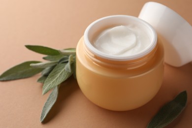Jar of face cream and sage leaves on beige background