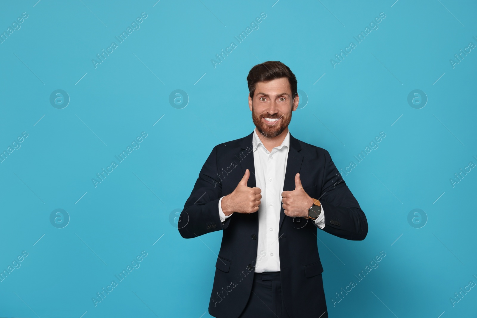 Photo of Smiling bearded man in suit showing thumbs up on light blue background