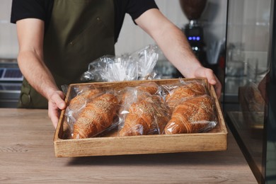 Photo of Seller with croissants at cashier desk in bakery shop, closeup