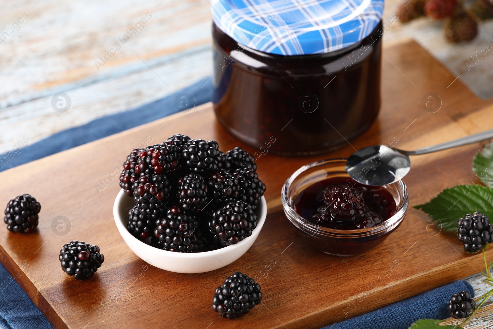 Photo of Fresh ripe blackberries, tasty jam and leaves on table, closeup