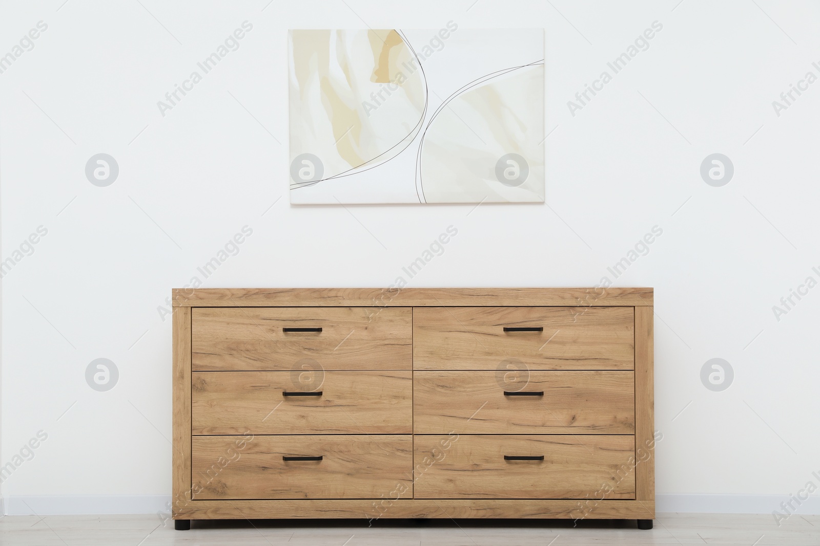 Photo of Wooden chest of drawers and beautiful picture on white wall indoors. Interior design