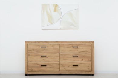 Wooden chest of drawers and beautiful picture on white wall indoors. Interior design