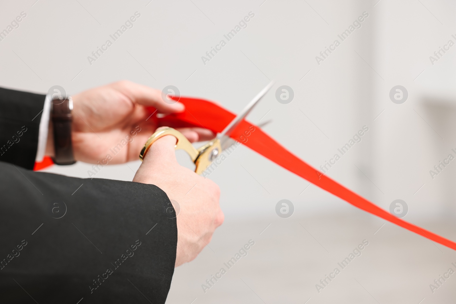 Photo of Woman cutting red ribbon with scissors indoors, closeup