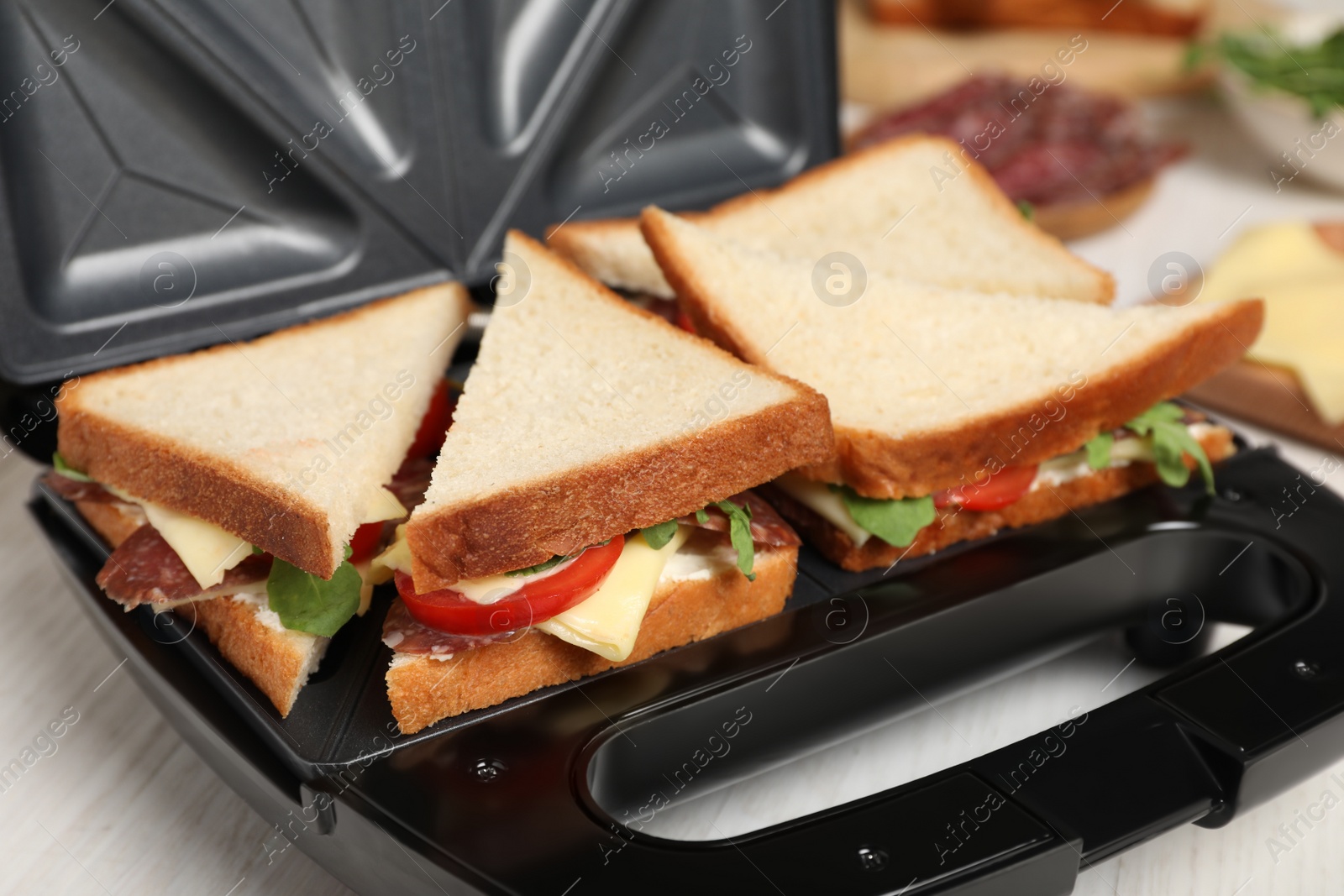 Photo of Modern grill maker with tasty sandwiches on white wooden table, closeup view