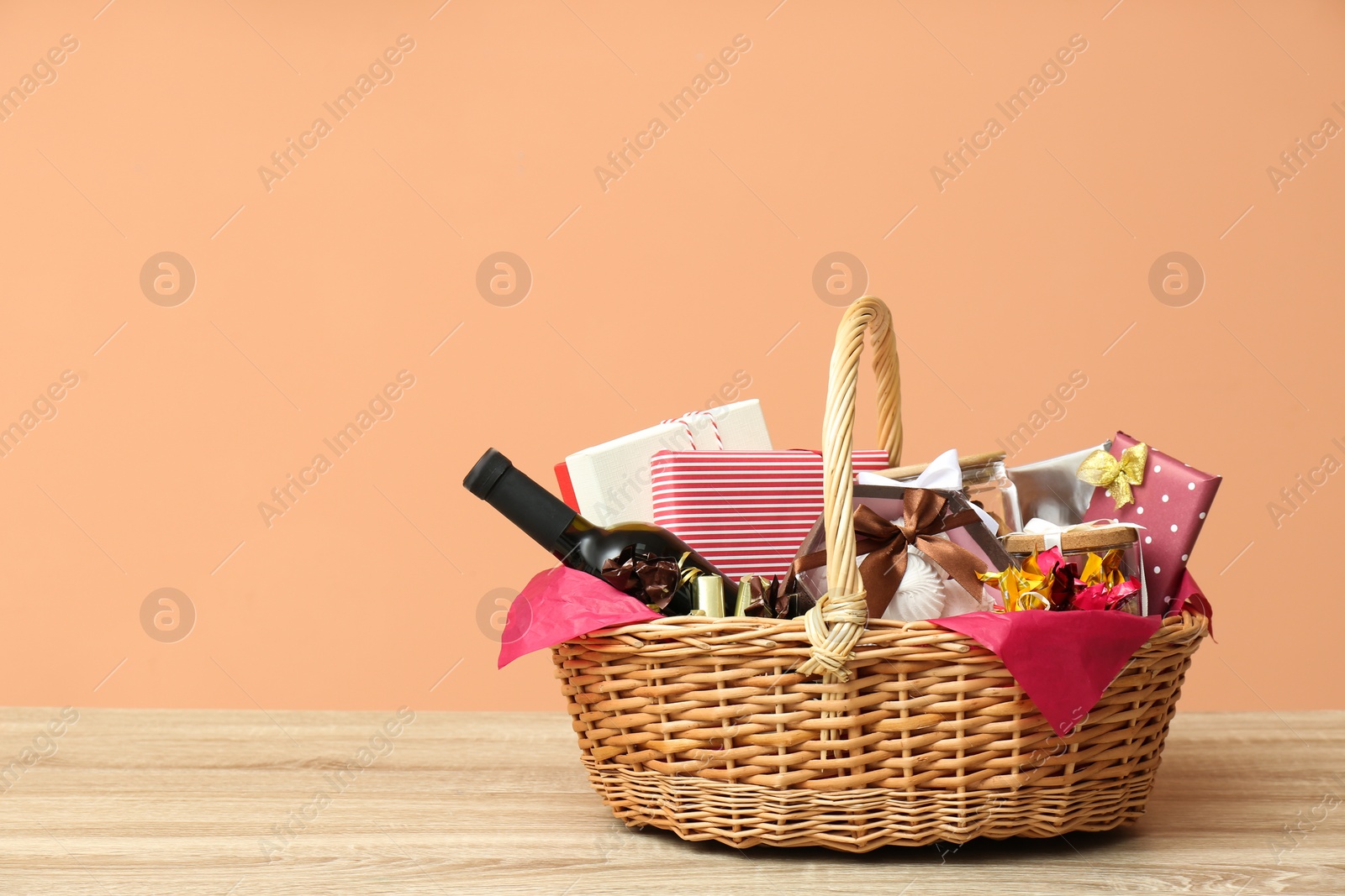 Photo of Wicker gift basket with bottle of wine on wooden table. Space for text