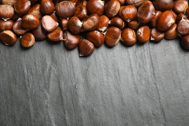 Photo of Fresh sweet edible chestnuts on black slate table, flat lay. Space for text
