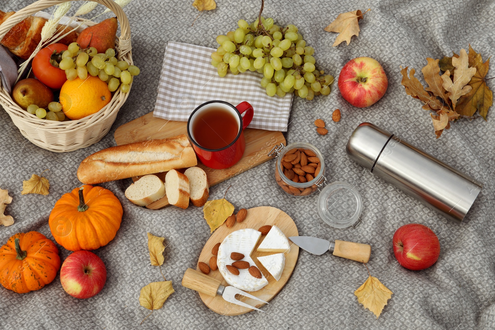 Photo of Blanket with picnic basket, snacks and autumn leaves, flat lay