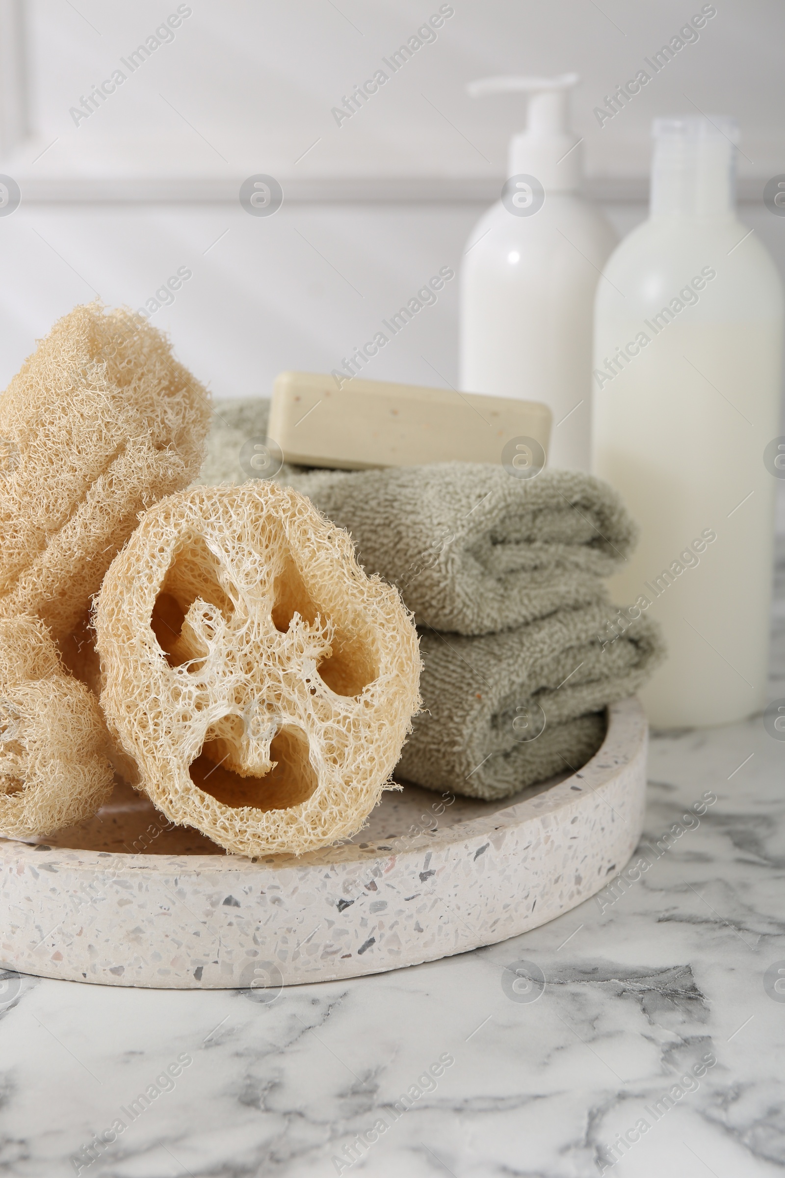 Photo of Loofah sponges, towels, soap and cosmetic products on white marble table