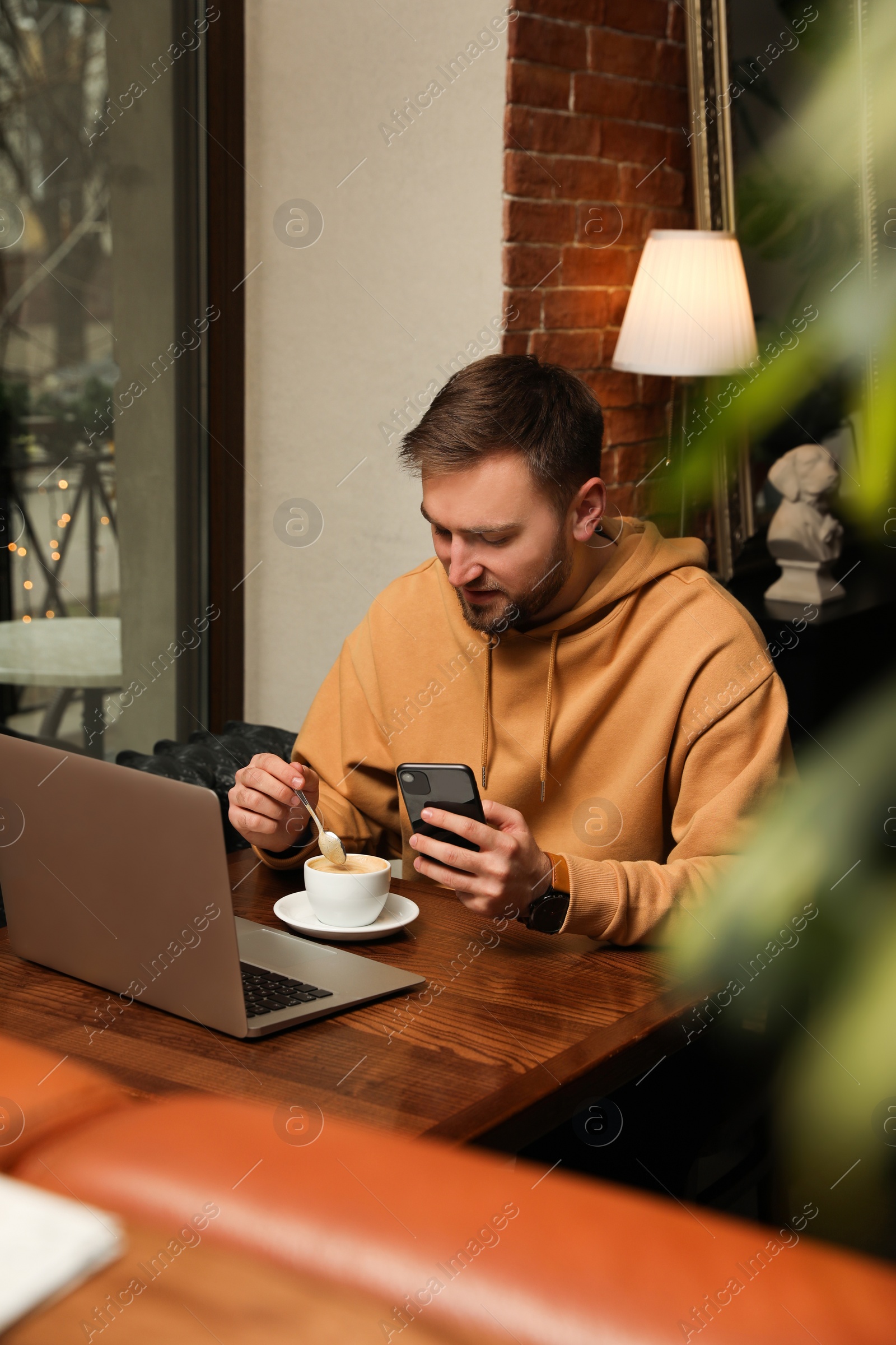 Photo of Male blogger with cup of coffee using phone at table in cafe